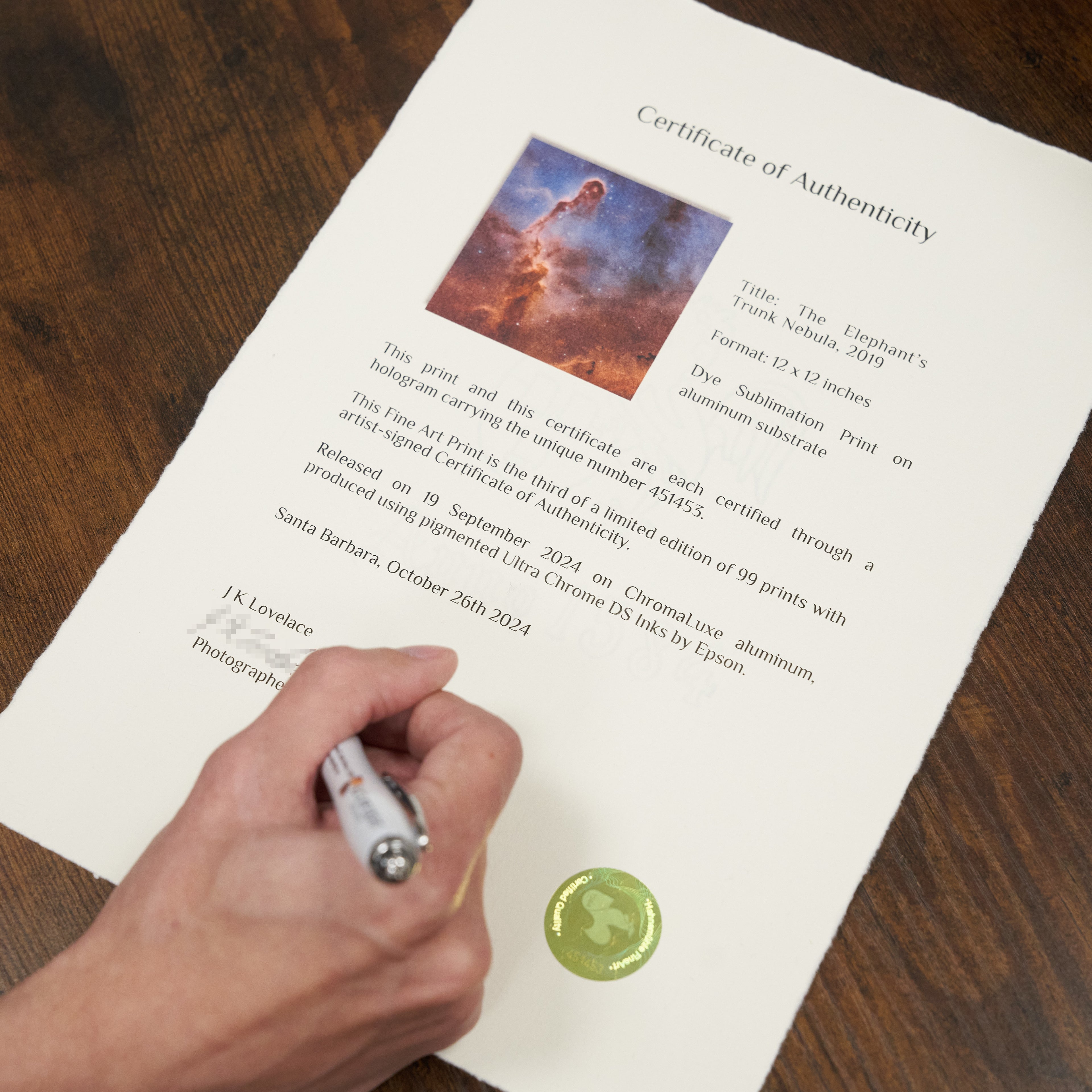 A detail shot of a Certificate of Authenticity with holographic serial sticker being signed.