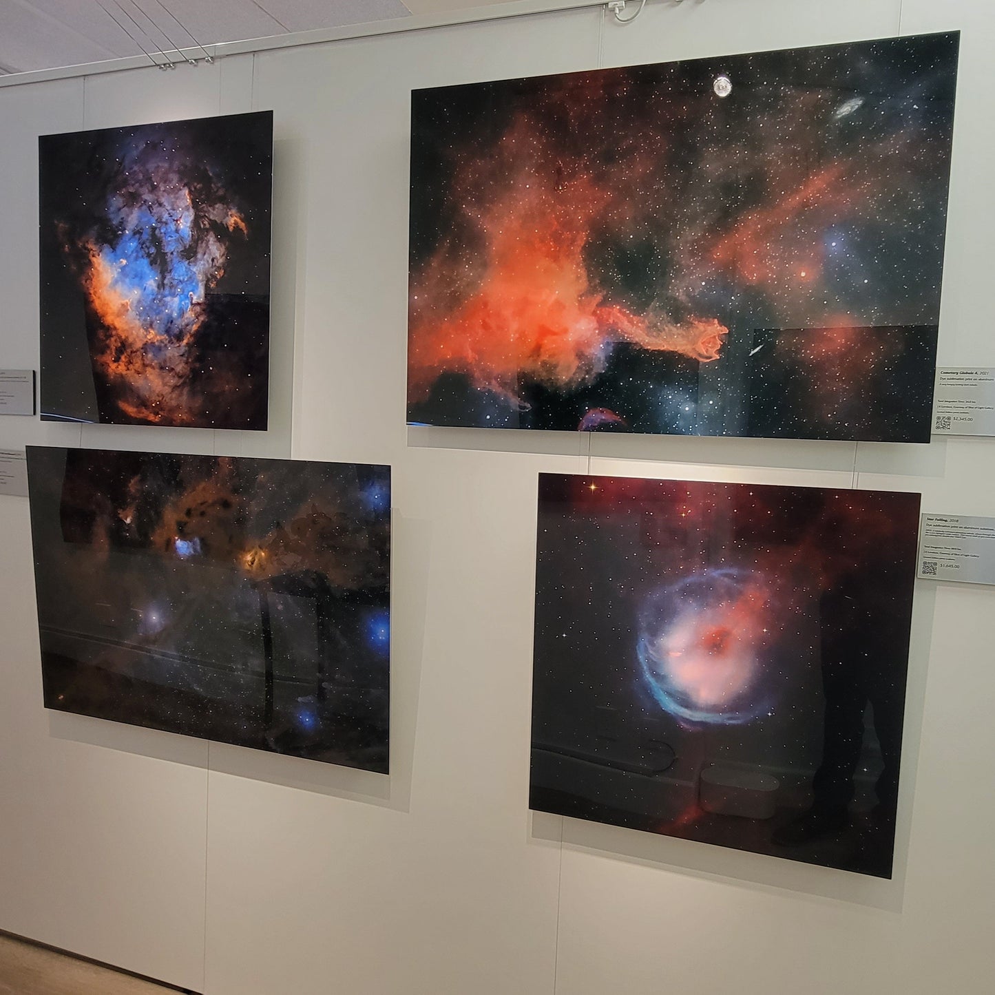 A photograph of the partition wall within Slice of Light Gallery dedicated to metal prints of deep sky objects, including the prints titled "Blue Heaven", "CG4", "Nebulas LBN 782 and Barnard 7", and "Star Falling".