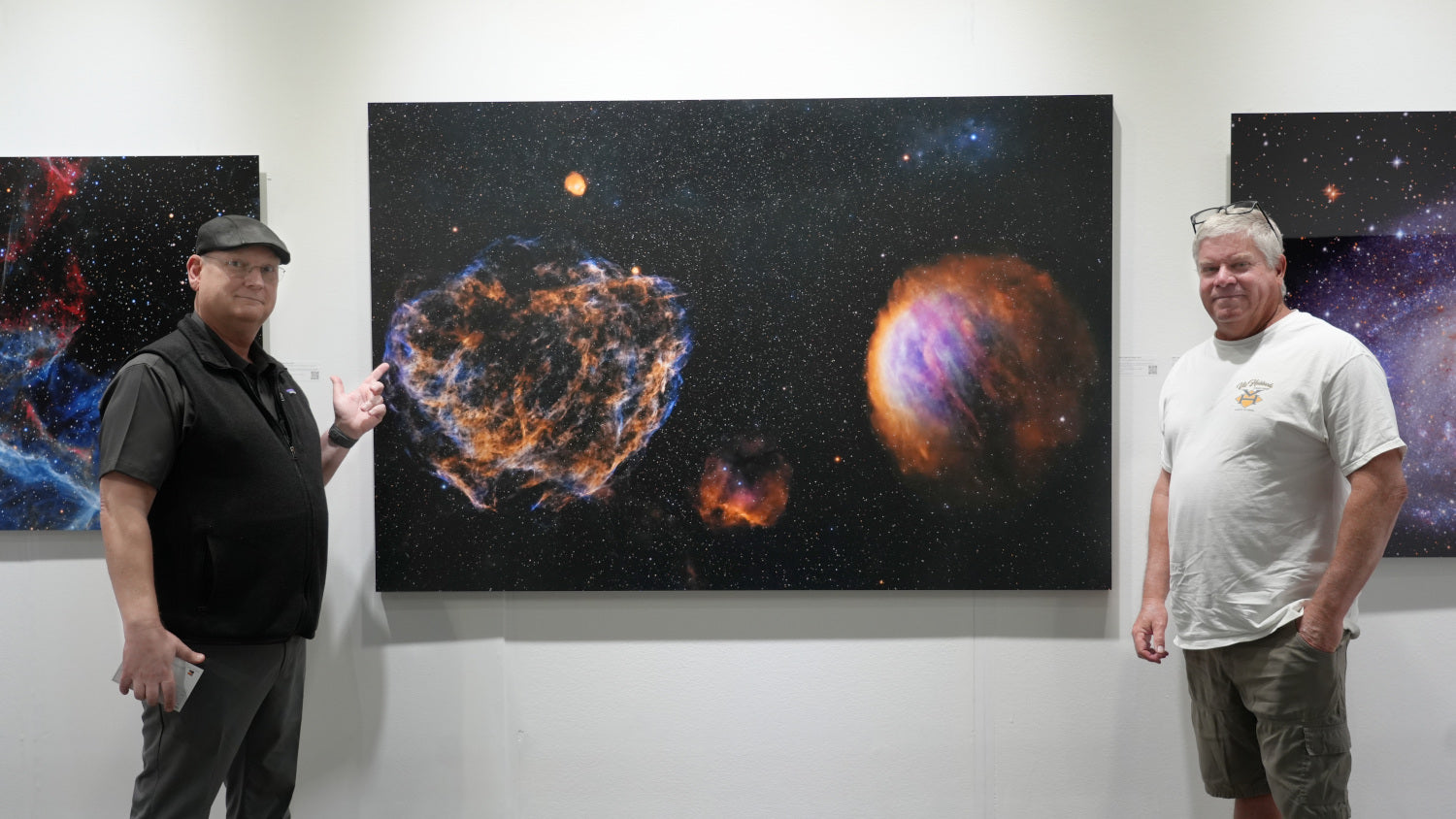 Two men standing in front of space-themed artwork in a gallery.
