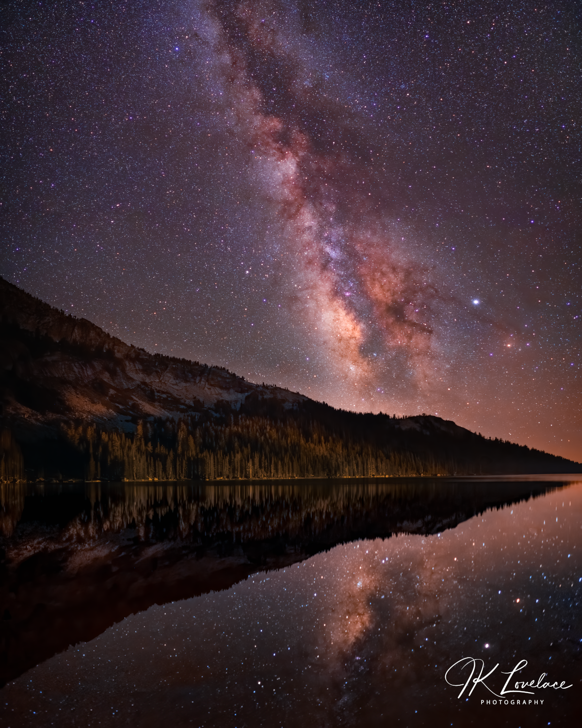 A png of the nightscape photograph titled, "High Lake" shot by astrophotographer J K Lovelace, featuring a vertical panorama of long exposures capturing the Milky Way stretching above an undisturbed Tenaya Lake, Yosemite.