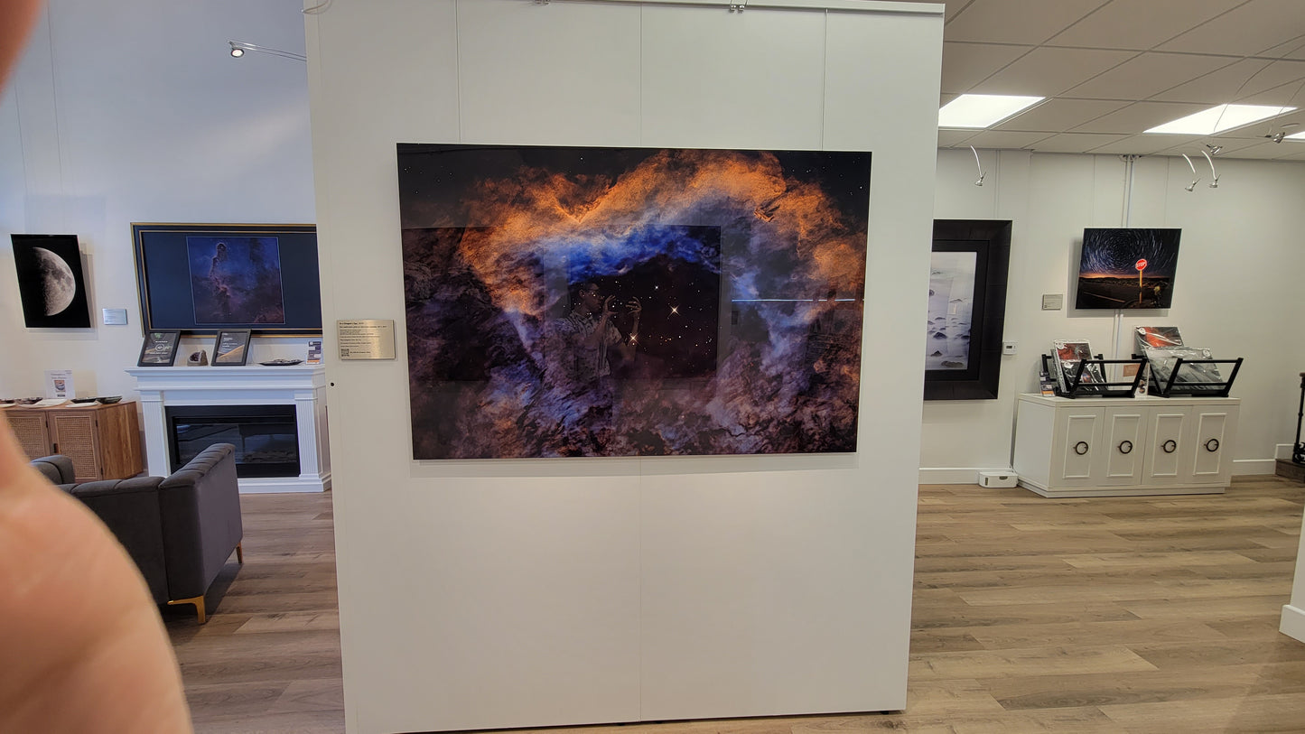 A photograph of the gallery interior showing the metal print titled "In A Dragon's Eye" on display. Other metal prints in view include "1st Quarter Moon" and "Strange Occurrences in the Desert".