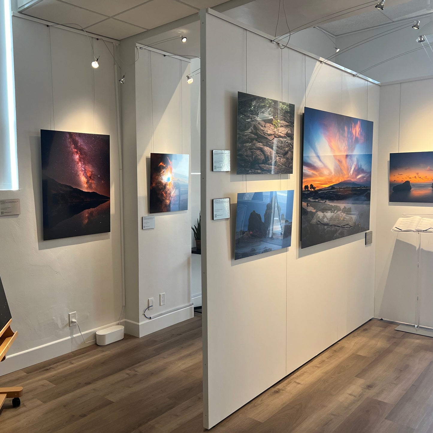 A photograph of the interior of Slice of Light Gallery taken from the vantage point of the manager's office, showing multiple metal prints on display on the walls and partitions.