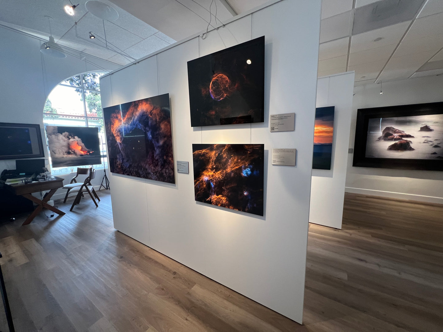 A photograph of the interior of Slice of Light Gallery, taken from the cosmic cove, showing mutliple metal prints and the sales desk.