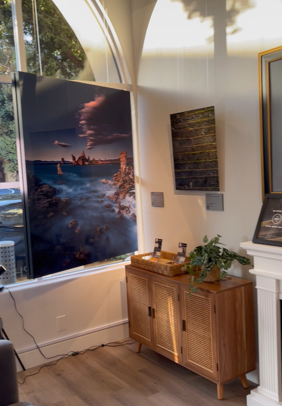 A photograph of the interior of Slice of Light Gallery, showing the metal prints titled "Mono Lith" and "Happy New Year" near the front window.