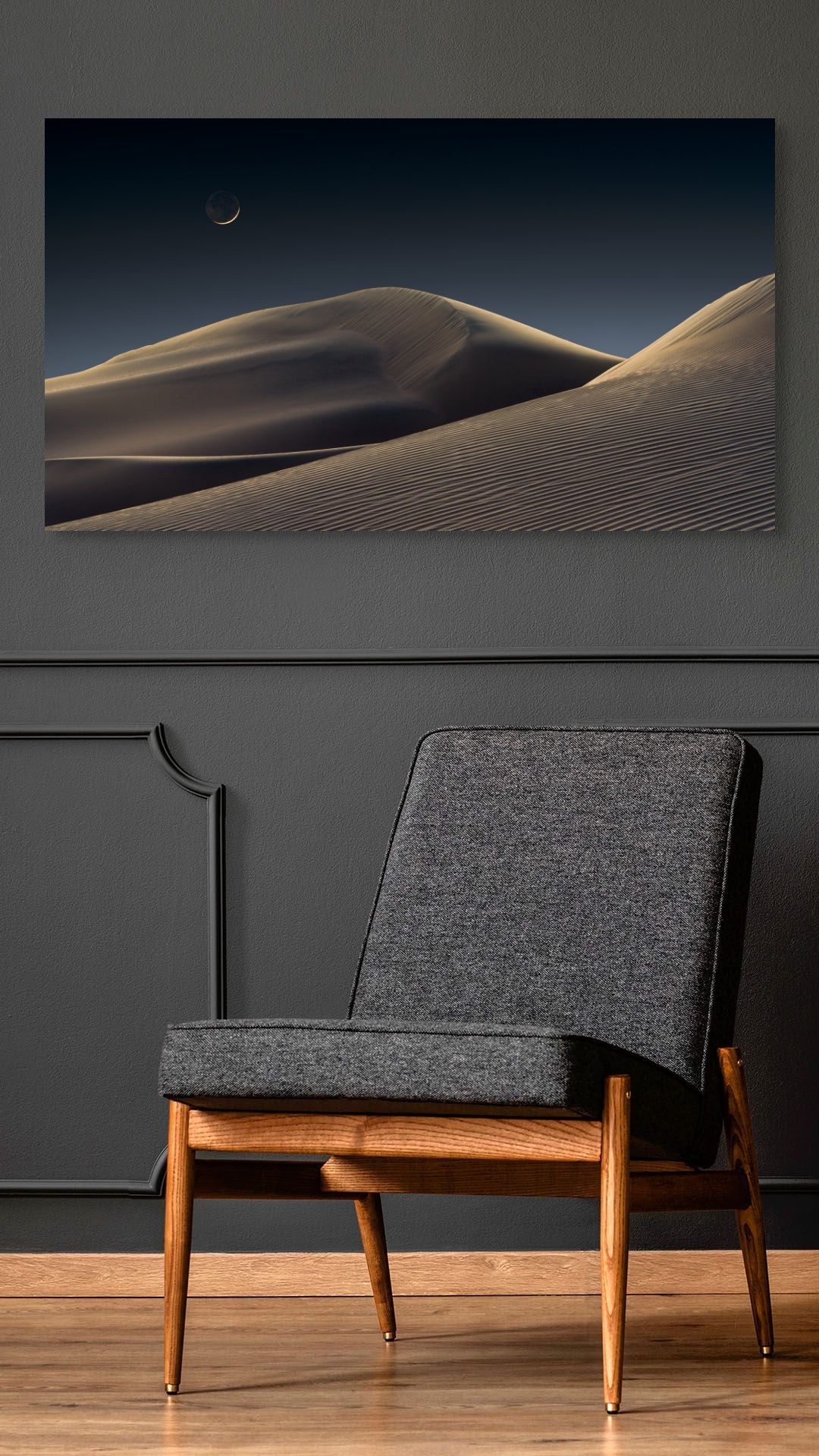 A wall art mockup featuring the photograph titled "Luna Dunes" by landscape photographer J K Lovelace as a 30 inch wide metal print with inset frame on dark wall above black chair.
