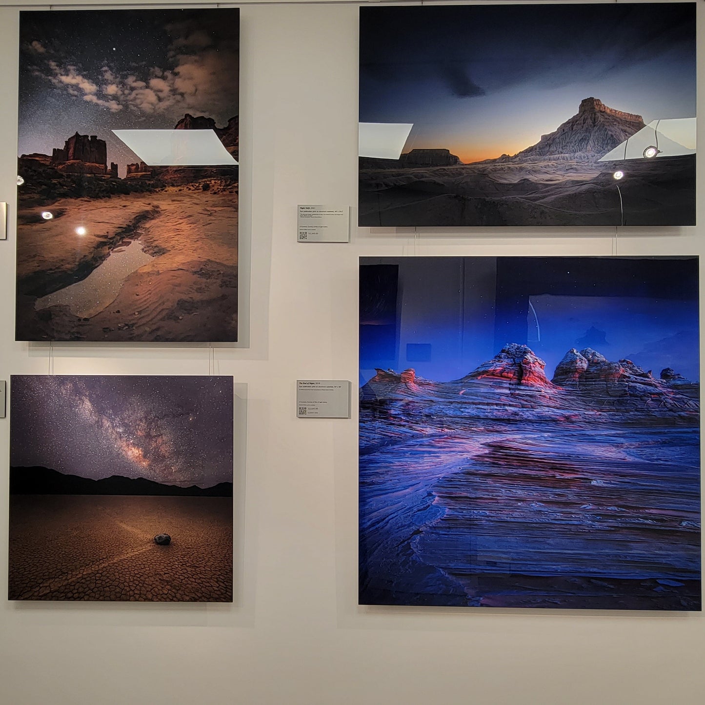 A photograph of the nightscape cove within Slice of Light Gallery, where the metal prints titled "A Fleeting Oasis", "Night Shift", "The Sailing Stone", and "The Red of Night" are on display.