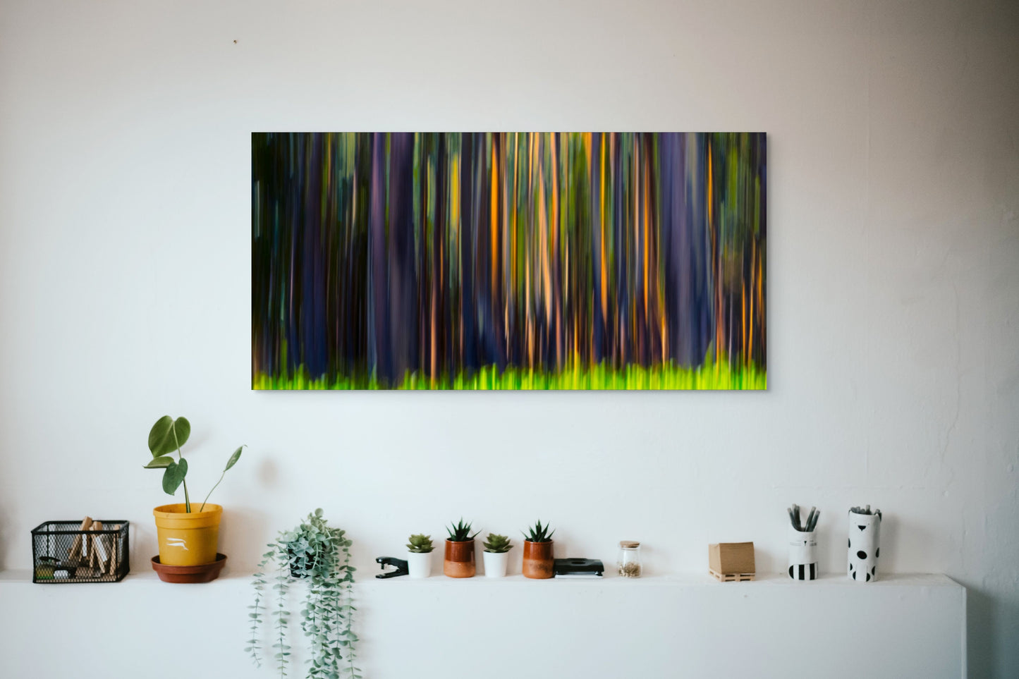 A wall art mockup featuring the photograph titled "Rainbow Eucalyptus, Big Island" by landscape photographer Ben Coffman as a 60 inch wide metal print with inset frame on display in a modern apartment.