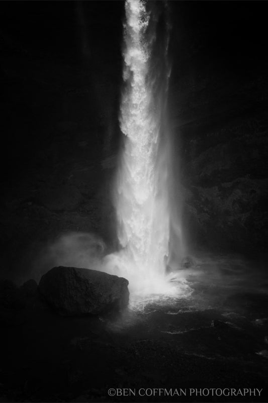 A jpg of the black and white photograph titled "Spring Waterfall, Iceland" by landscape photographer Ben Coffman, featuring the 100-foot waterfall Kvernufoss slams into a rock at its base, Iceland.