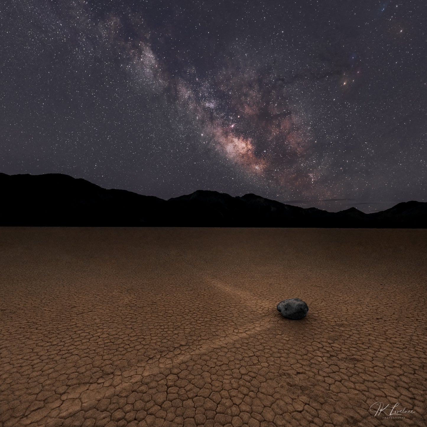 A jpg of the nightscape photograph titled "The Sailing Stone" shot by landscape photographer J K Lovelace featuring a lone racing stone with two tracks on the Racetrack Playa in Death Valley