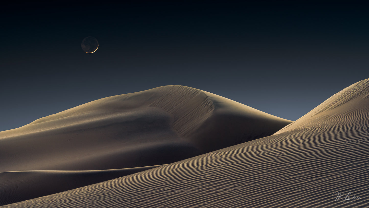 A jpg of the award winning photograph titled, "Luna Dunes" shot by landscape photographer J K Lovelace, featuring a smoldering crescent moon floating in an undisturbed atmosphere above quiet, glowing dunes.