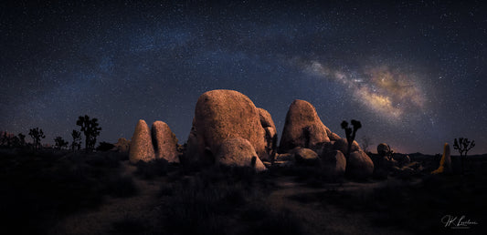 A jpg of the nightscape photograph titled "The Stones of Joshua" shot by landscape photographer J K Lovelace featuring the stars and Milky Way Core rising over eerie monolithic desert stones and Joshua Trees in Joshua Tree National Park.