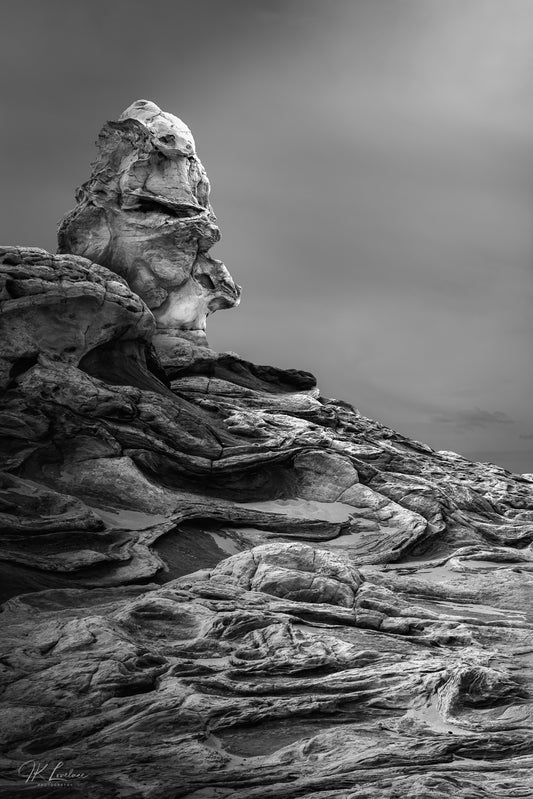 A jpg of the black and white landscape photograph titled "The Watchers 1 - Anaye" shot by landscape photographer J K Lovelace featuring a pareidolic rock formation found in Vermillion Cliffs National Monument