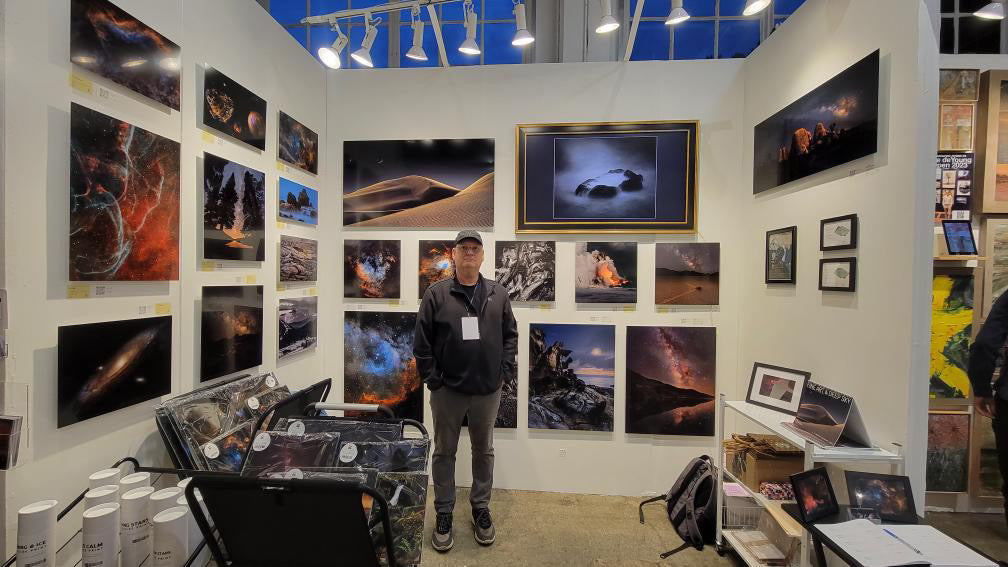 Person standing in a gallery with various framed artworks on the walls.