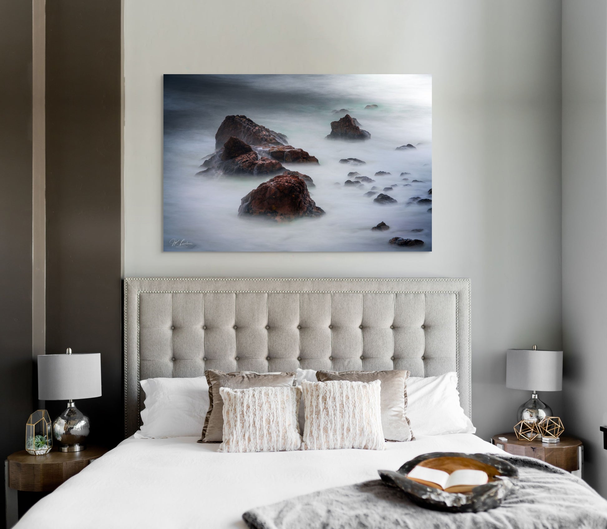 A wall art mockup featuring the photograph titled "Beyond Here Be Dragons" by landscape photographer J K Lovelace as a 60 inch wide metal print with inset frame on display in a California coastal bedroom.