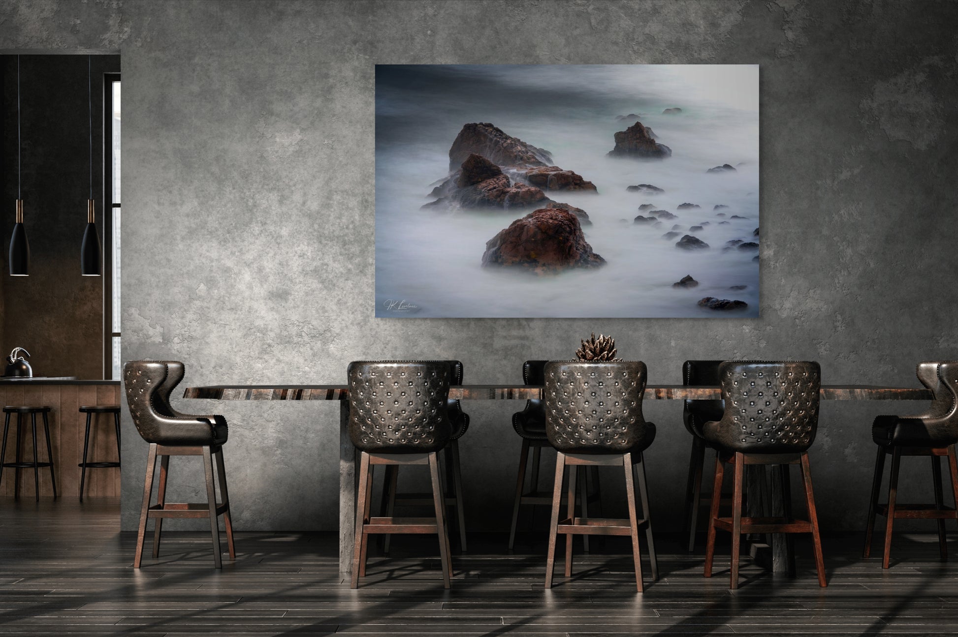 A wall art mockup featuring the photograph titled "Beyond Here Be Dragons" by landscape photographer J K Lovelace as a 60 inch wide metal print with inset frame on display in an industrial dining room.