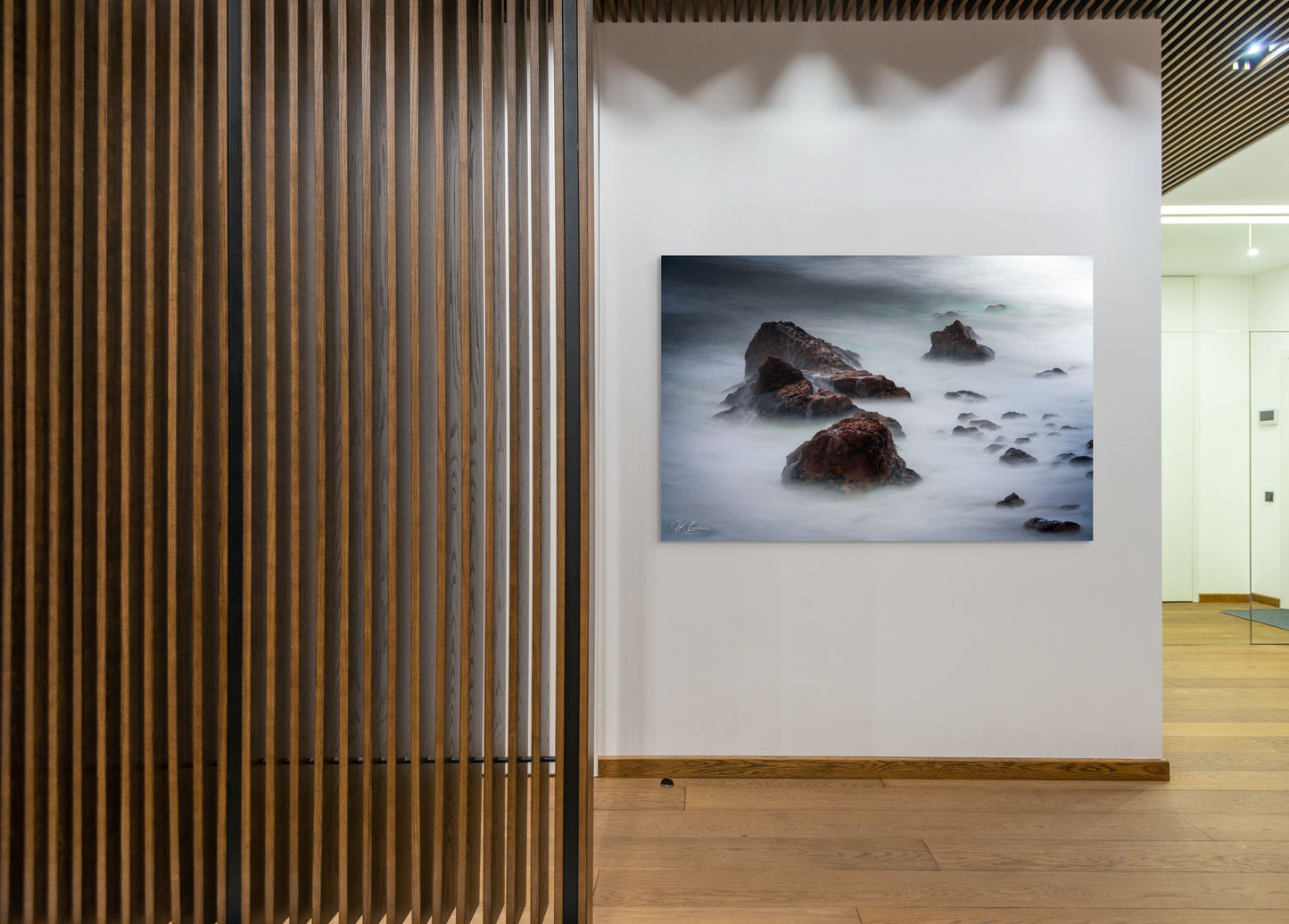 A wall art mockup featuring the photograph titled "Beyond Here Be Dragons" by landscape photographer J K Lovelace as a 60 inch wide metal print with inset frame on display in a modern university.