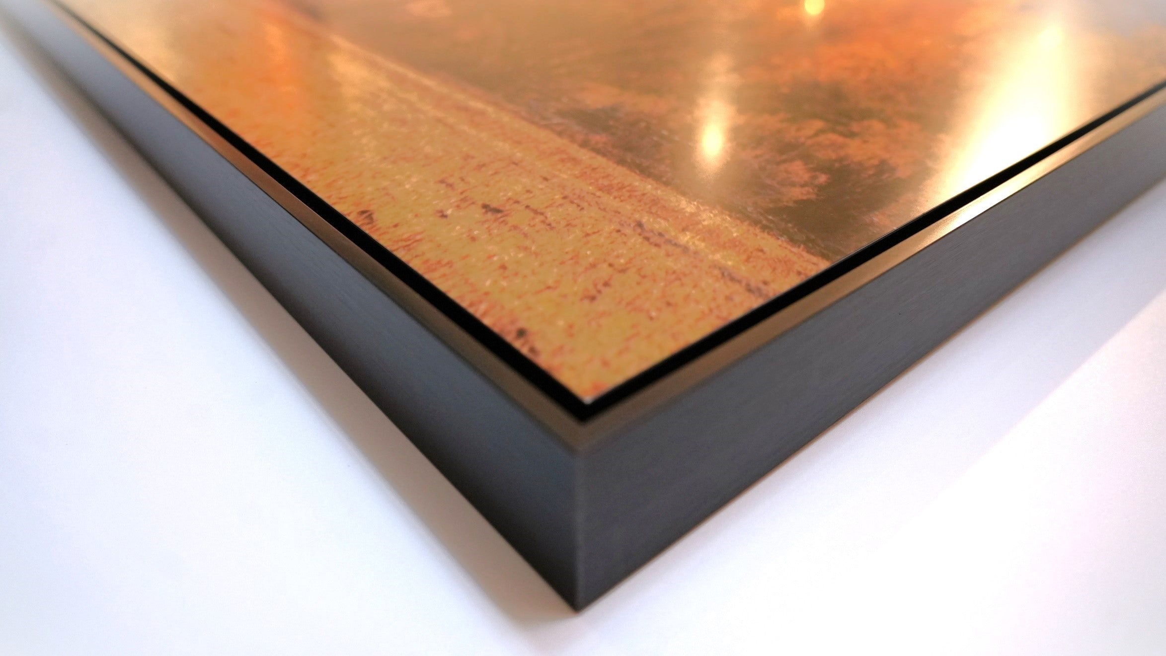 A photograph of the corner of a shadow box frame, showing the gap between the metal print and metal frame.