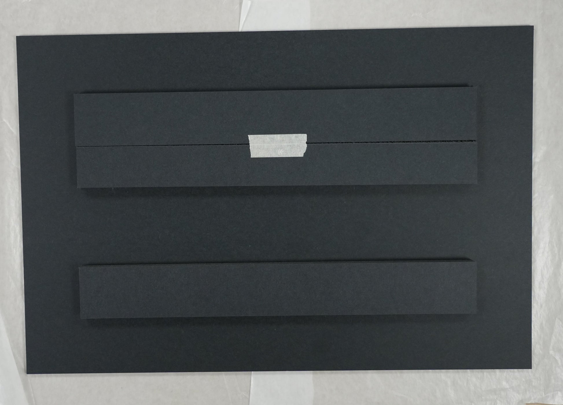 Black rectangular object on a white sheet with a ruler for scale on a beige background
