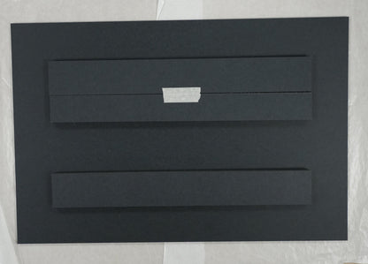 Black rectangular object on a white sheet with a ruler for scale on a beige background