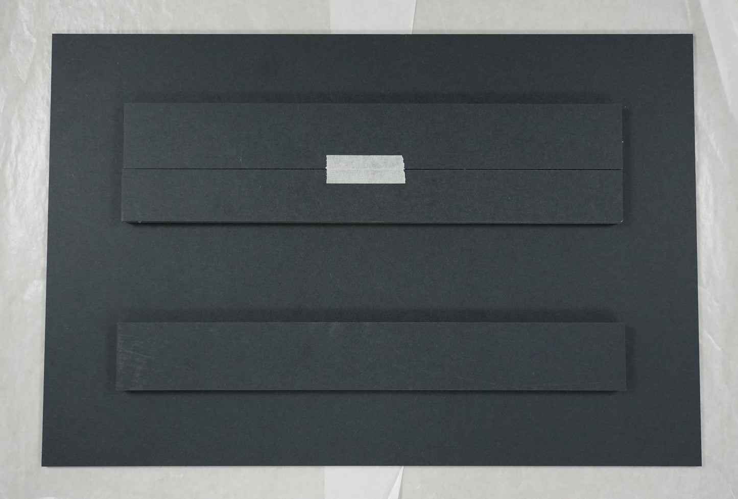 Black rectangular object on a white sheet of paper with a ruler for scale.