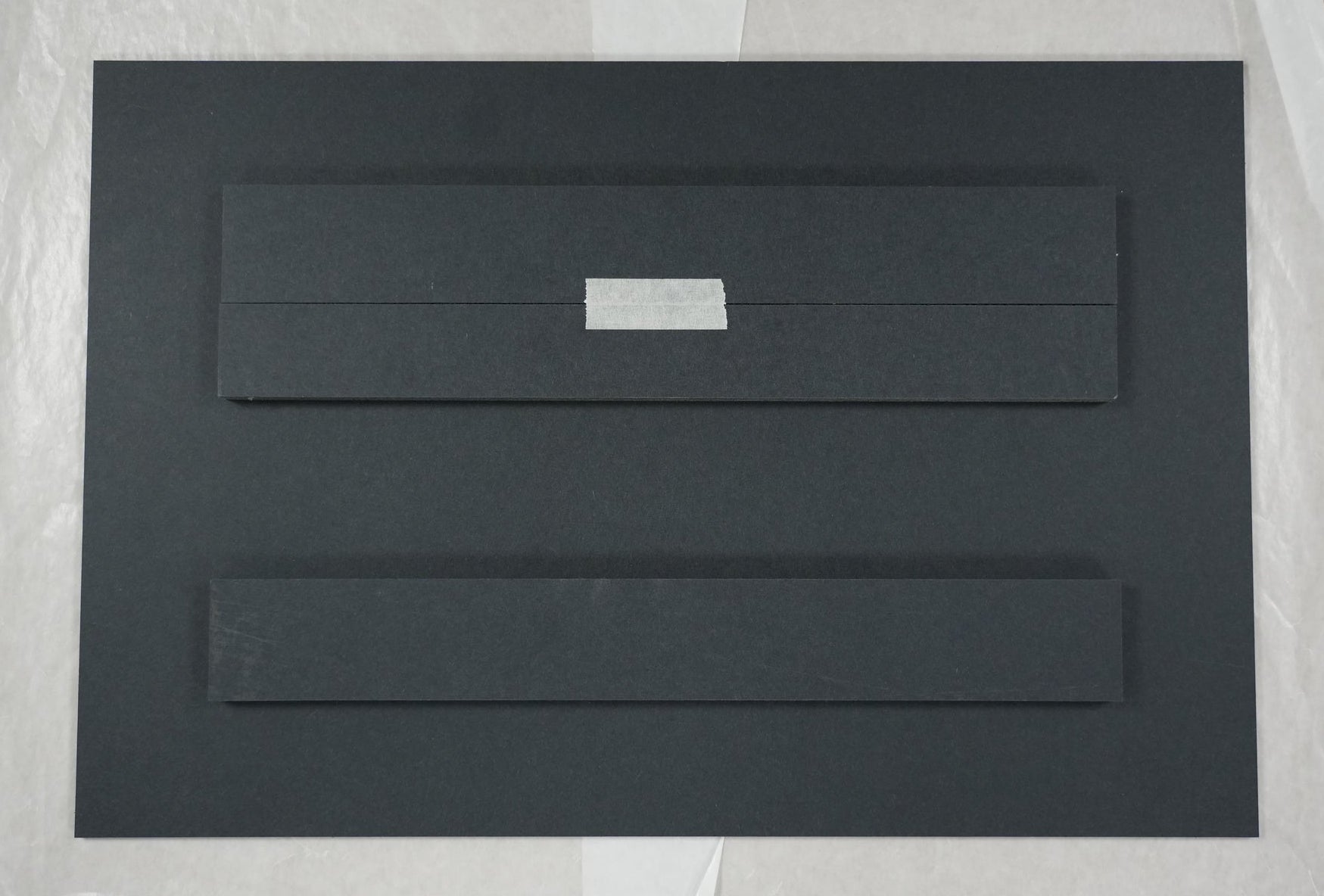 Black rectangular object on a white sheet of paper with a ruler for scale.