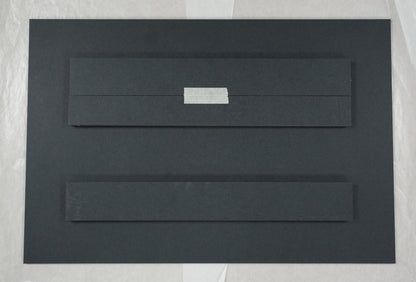 Black rectangular object on a white sheet of paper with a ruler for scale.