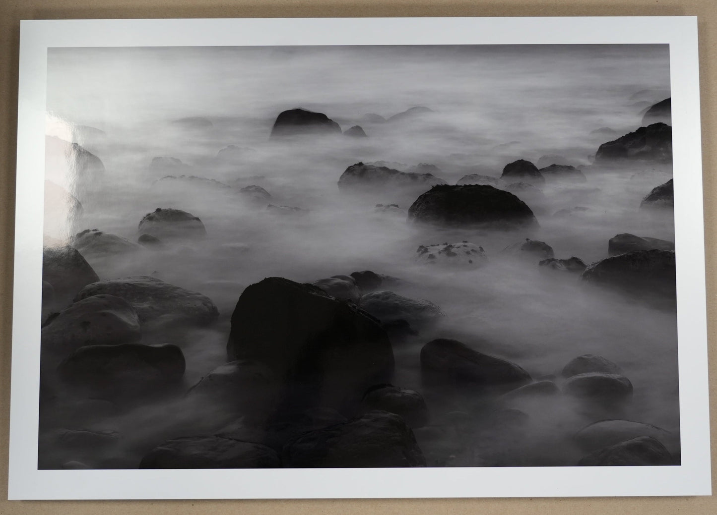 Framed black and white artwork of rocks and water on a beige wall.