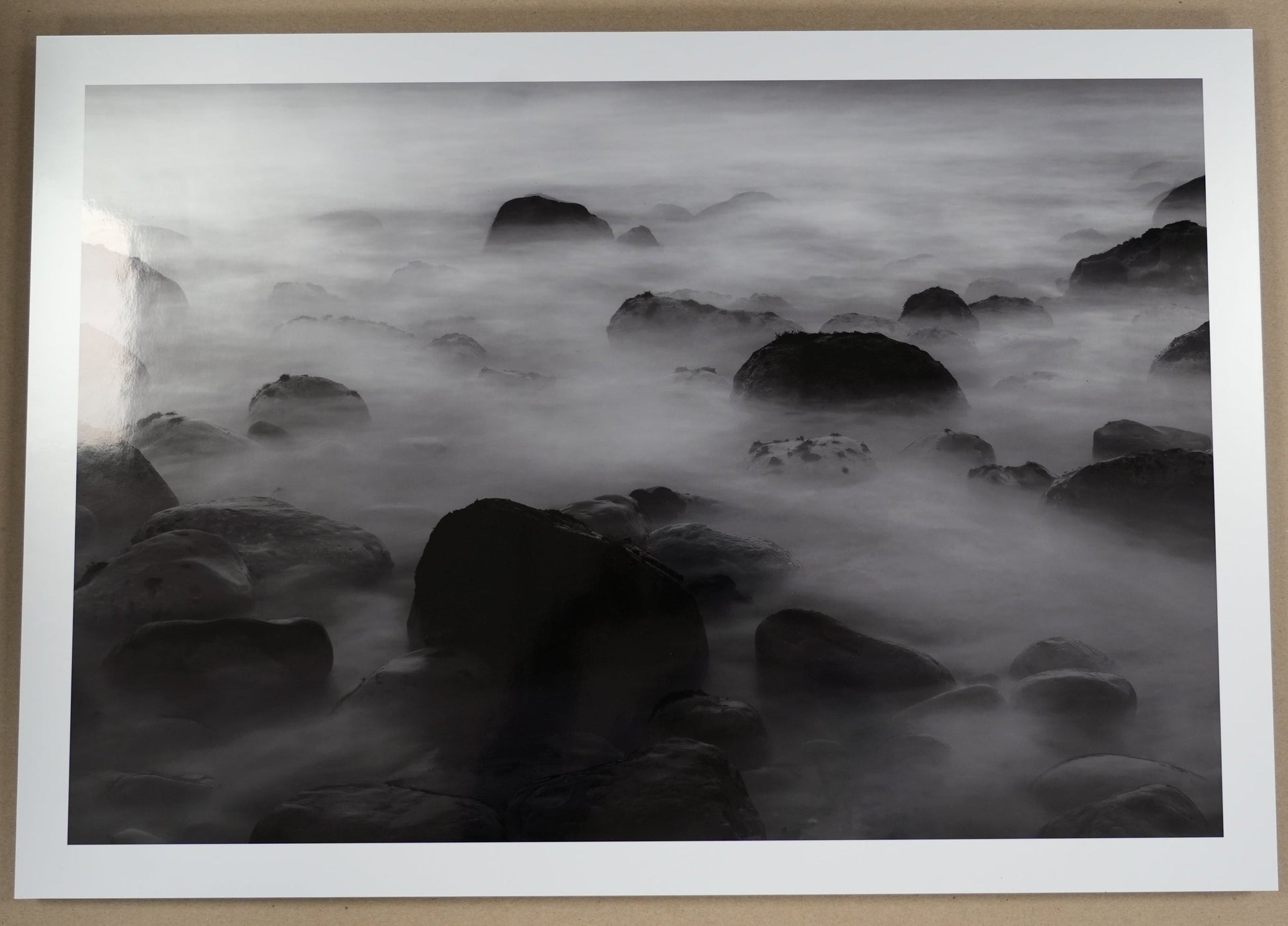 Framed black and white artwork of rocks and water on a beige wall.