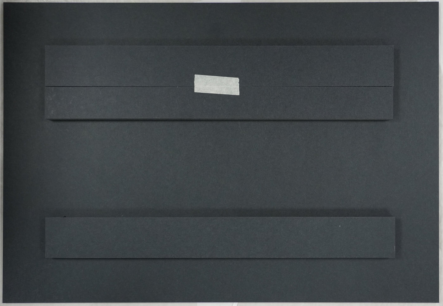 Black rectangular object with a white label on a beige surface, with a ruler for scale.