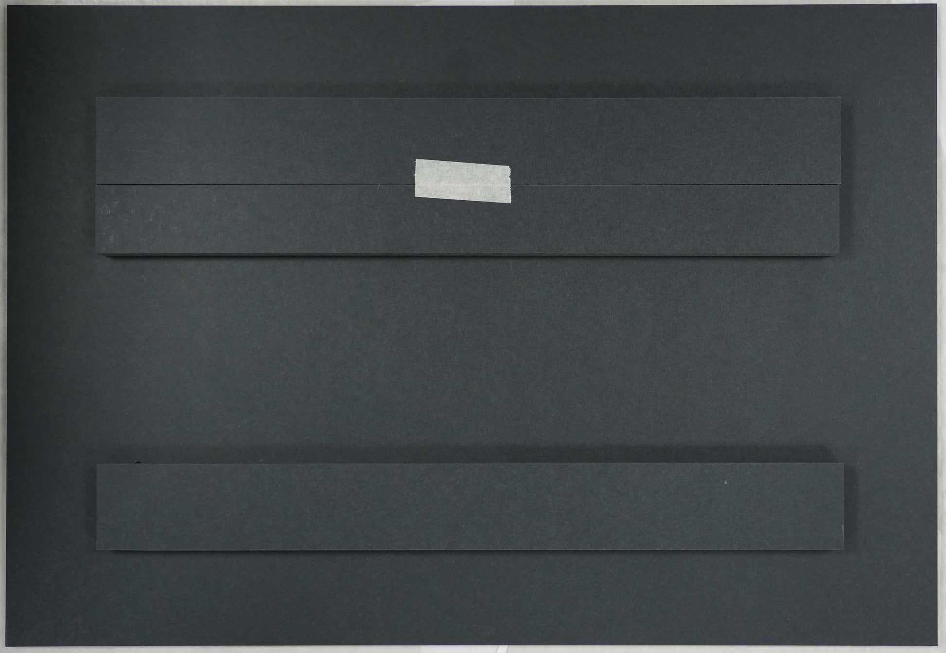 Black rectangular object with a white label on a beige surface, with a ruler for scale.