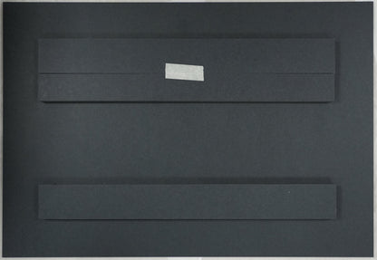 Black rectangular object with a white label on a beige surface, with a ruler for scale.