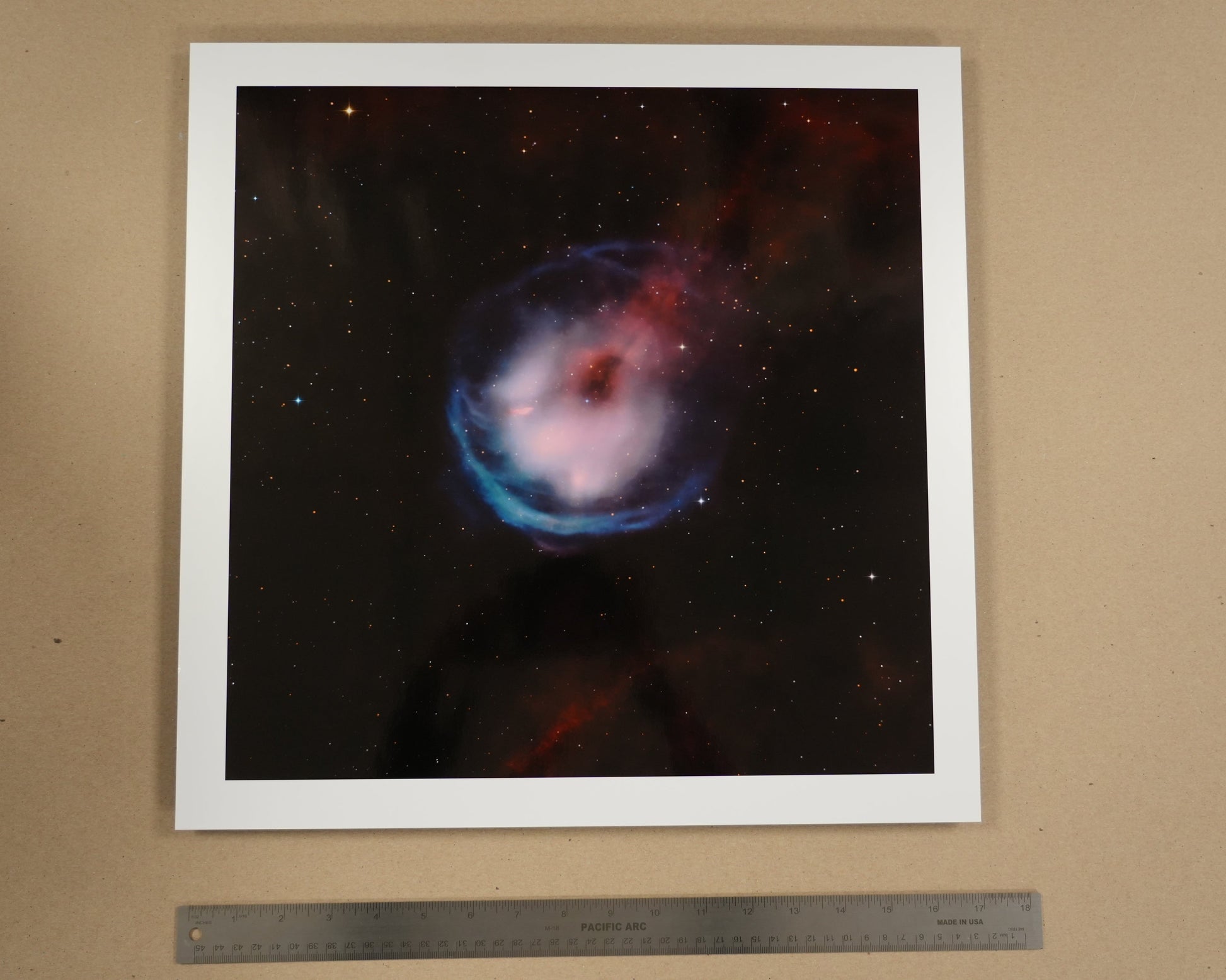 Framed photograph of a nebula on a beige wall with a ruler below.