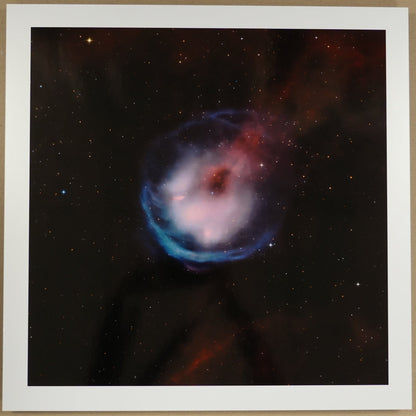 Framed photograph of a nebula on a beige wall with a ruler below.