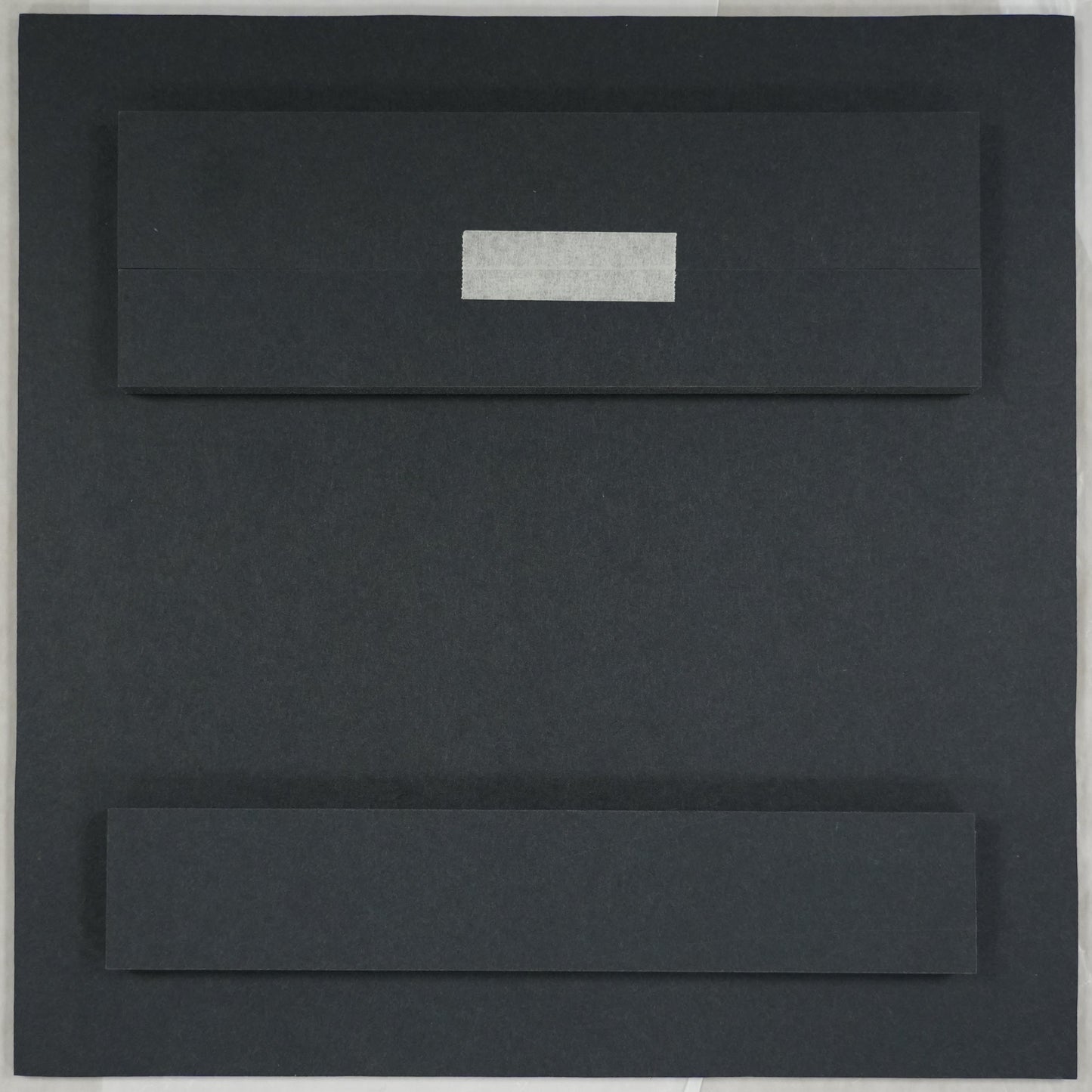 Black rectangular object on a white sheet of paper with a ruler at the bottom.
