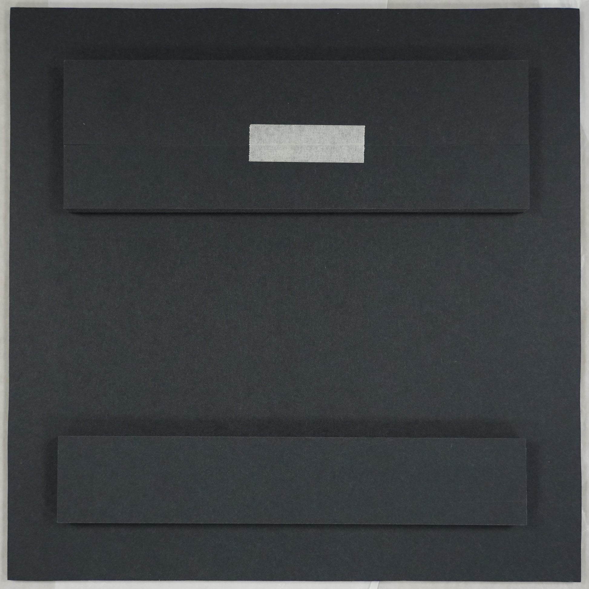 Black rectangular object on a white sheet of paper with a ruler at the bottom.