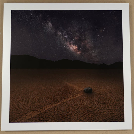 Framed photograph of a desert landscape with a starry night sky, placed on a beige surface.