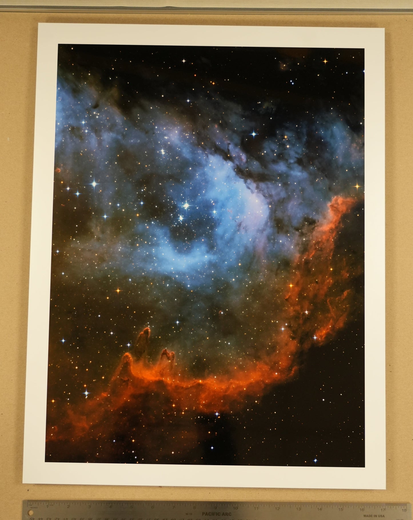 Framed photograph of a nebula with a ruler for scale on a wooden surface.