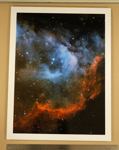 Framed photograph of a nebula with a ruler for scale on a wooden surface.