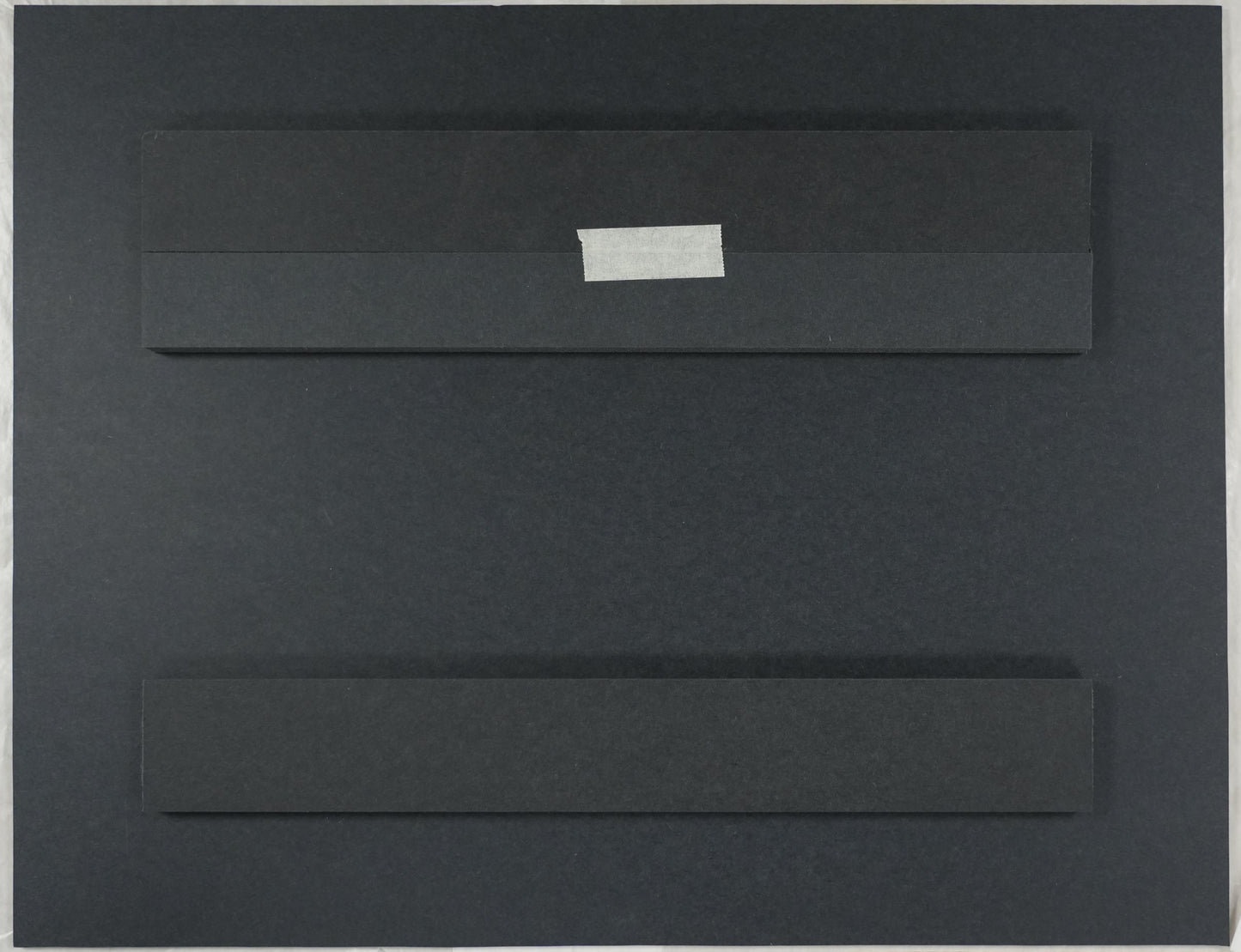 Black rectangular object on a beige surface with a ruler and scissors in the background