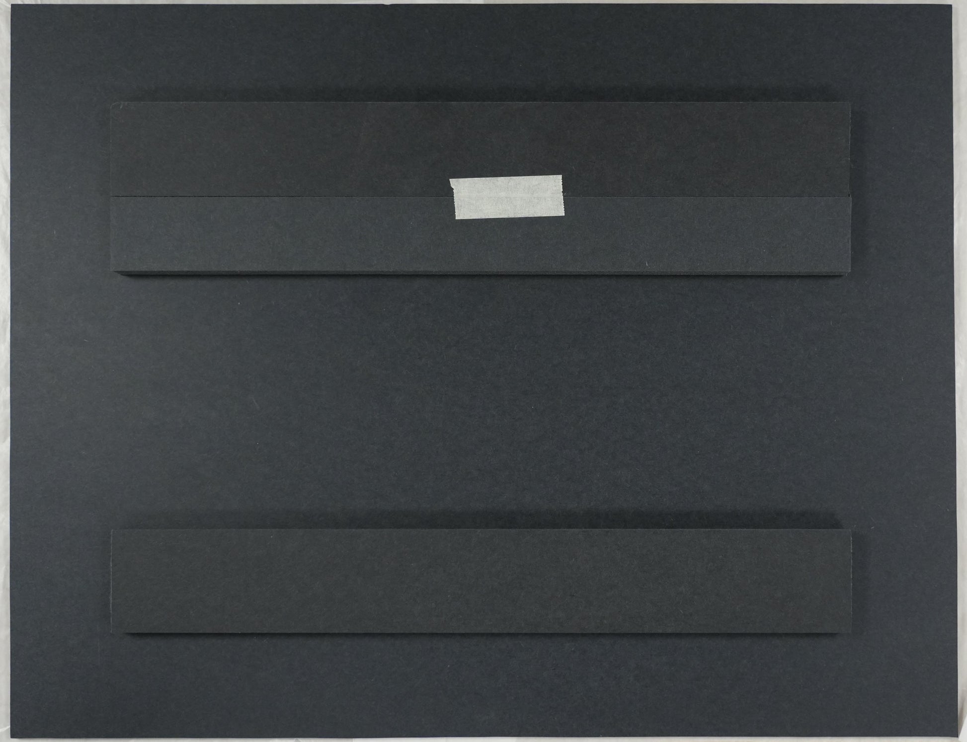Black rectangular object on a beige surface with a ruler and scissors in the background