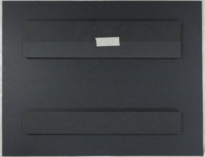 Black rectangular object on a beige surface with a ruler and scissors in the background