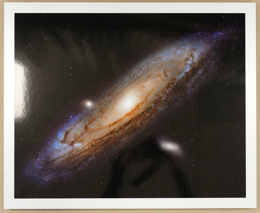 Framed photograph of a galaxy on a beige surface with a ruler and scissors in the background.