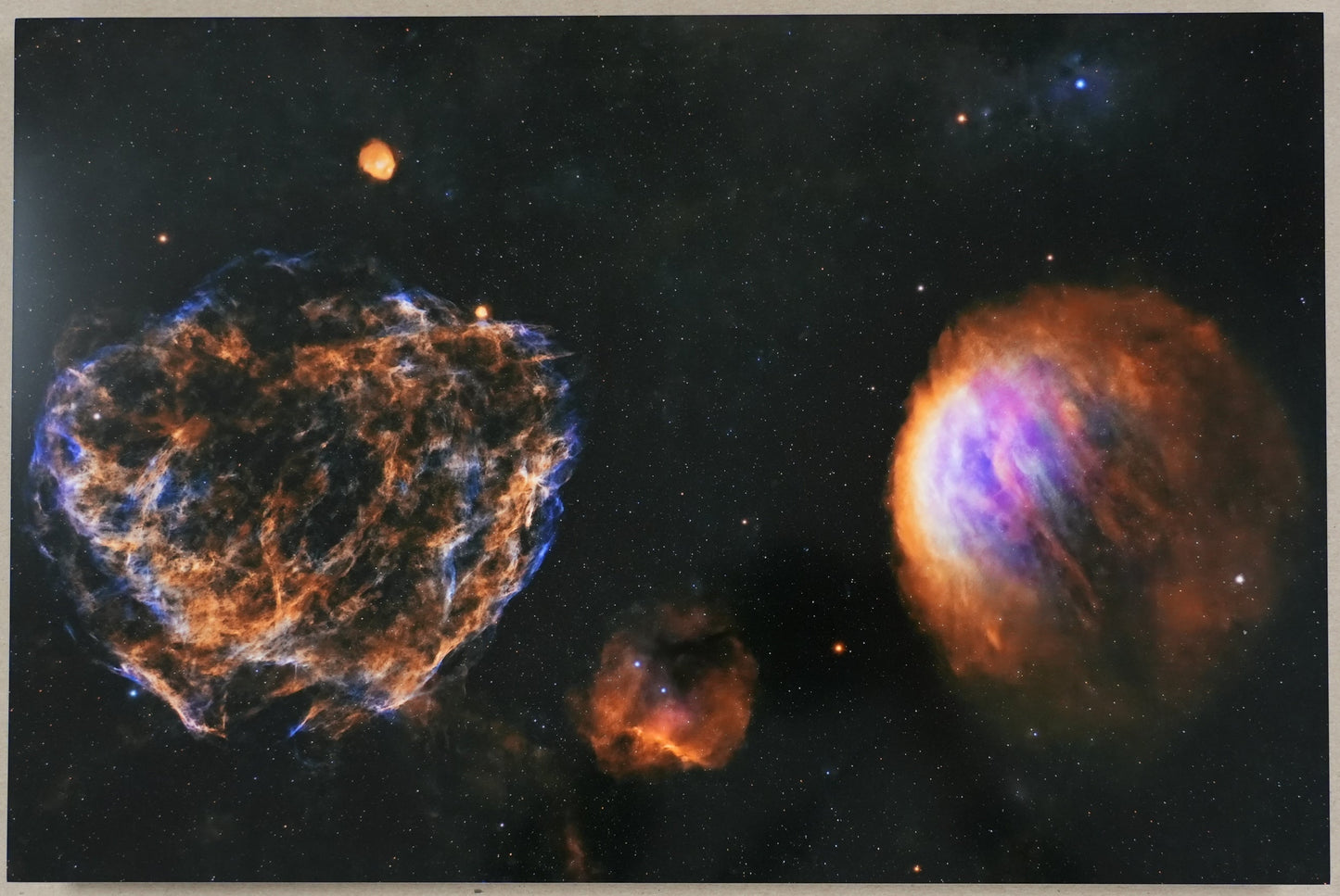 Framed space-themed artwork with nebulae and a ruler for scale on a plain wall.