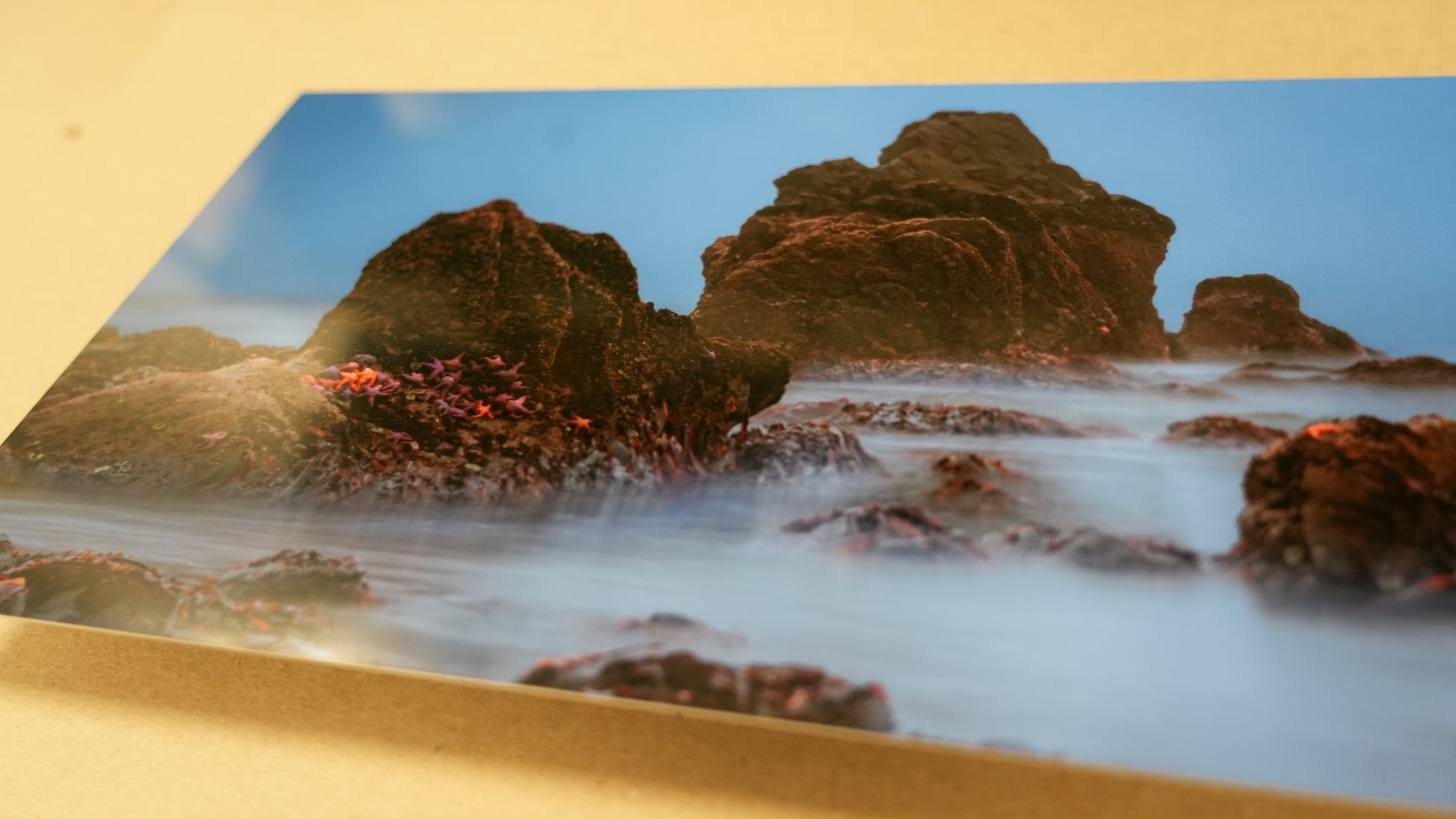Rocks on a beach with a blue sky, displayed on a gold background