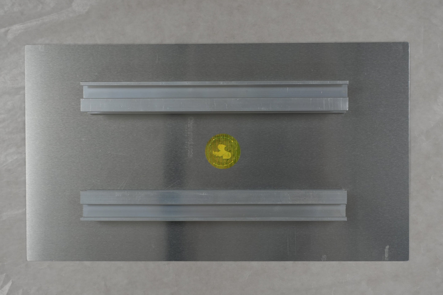 Rectangular metallic object with a yellow circle on a textured surface, with a ruler at the bottom.