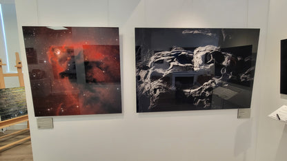 A photograph of the gallery interior showing the metal prints titled "Elmo's Ghost" and "The Skull of Ozymandias" on display on a wall partition.