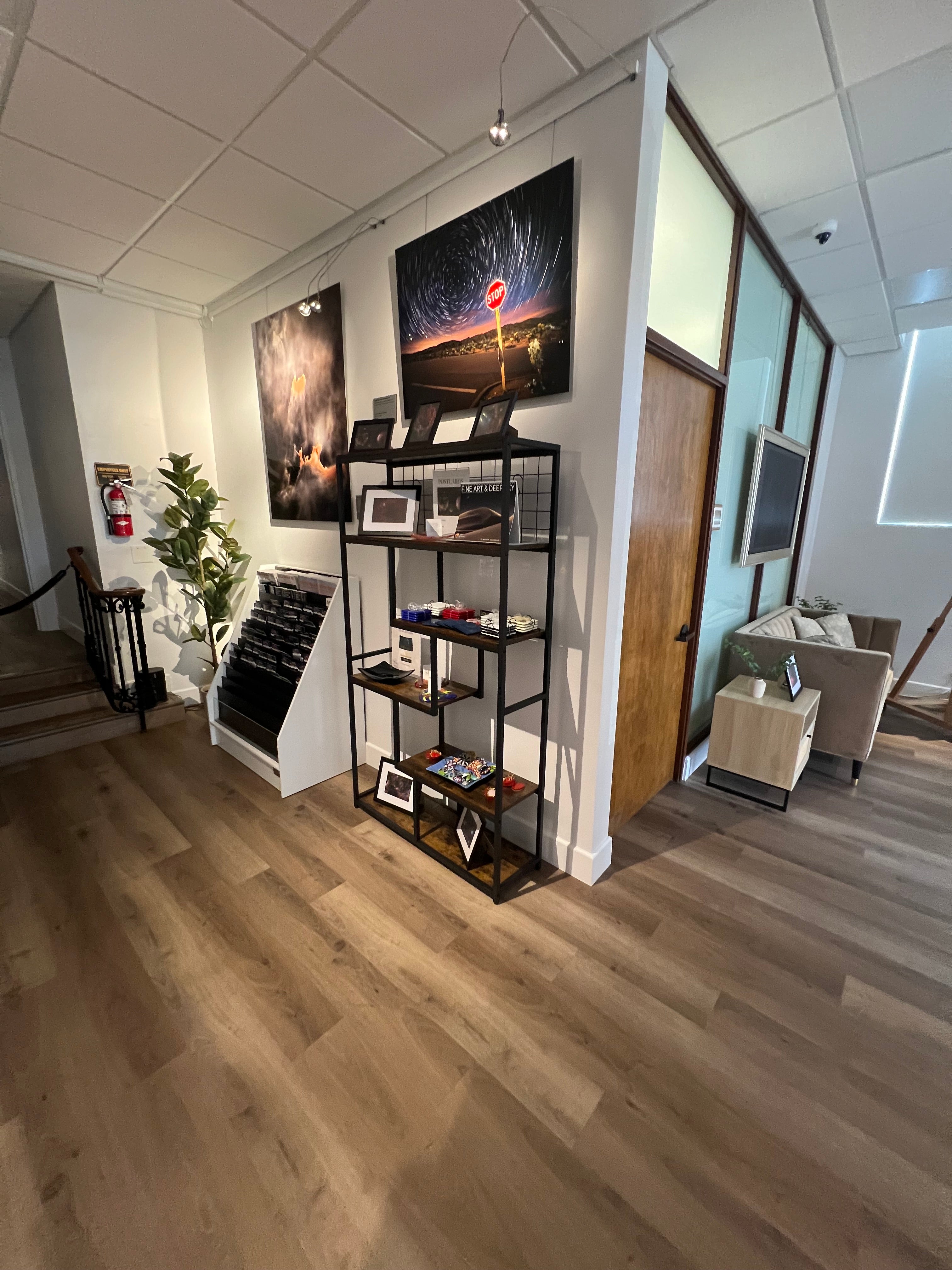 A photograph of the gallery interior facing the gift shop and the manager's office, with the metal prints titled "Strange Occurrences in the Desert" and "Andromeda Beseeches Perseus" on display.