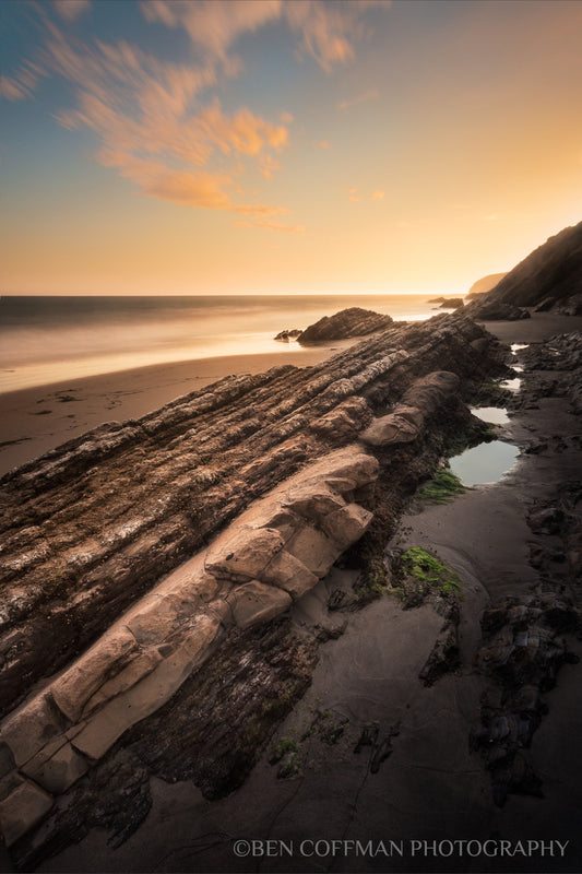 A jpg of a vertical photograph titled "Gaviota Sunset" shot by landscape photographer Ben Coffman, featuring clouds streak over rock ridges (Monterey formations) at sunset, Gaviota State Park, California.