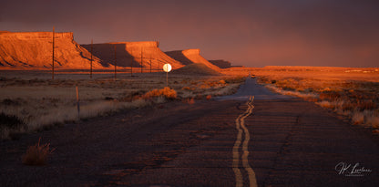 A jpg of the grand scenic photograph titled "Heading Home" shot by landscape photographer J K Lovelace, featuring desert plateaus and a lone truck along a highway.