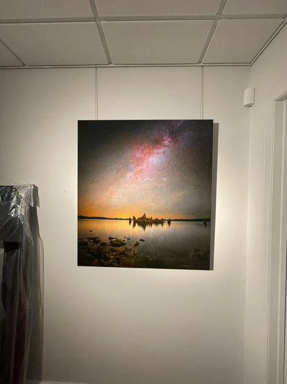 Framed artwork of a landscape with a starry sky and body of water on a white wall.